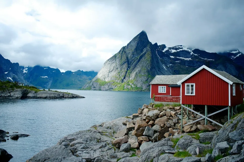 Rød hytte på stolper ved fjorden med fjell i bakgrunnen
